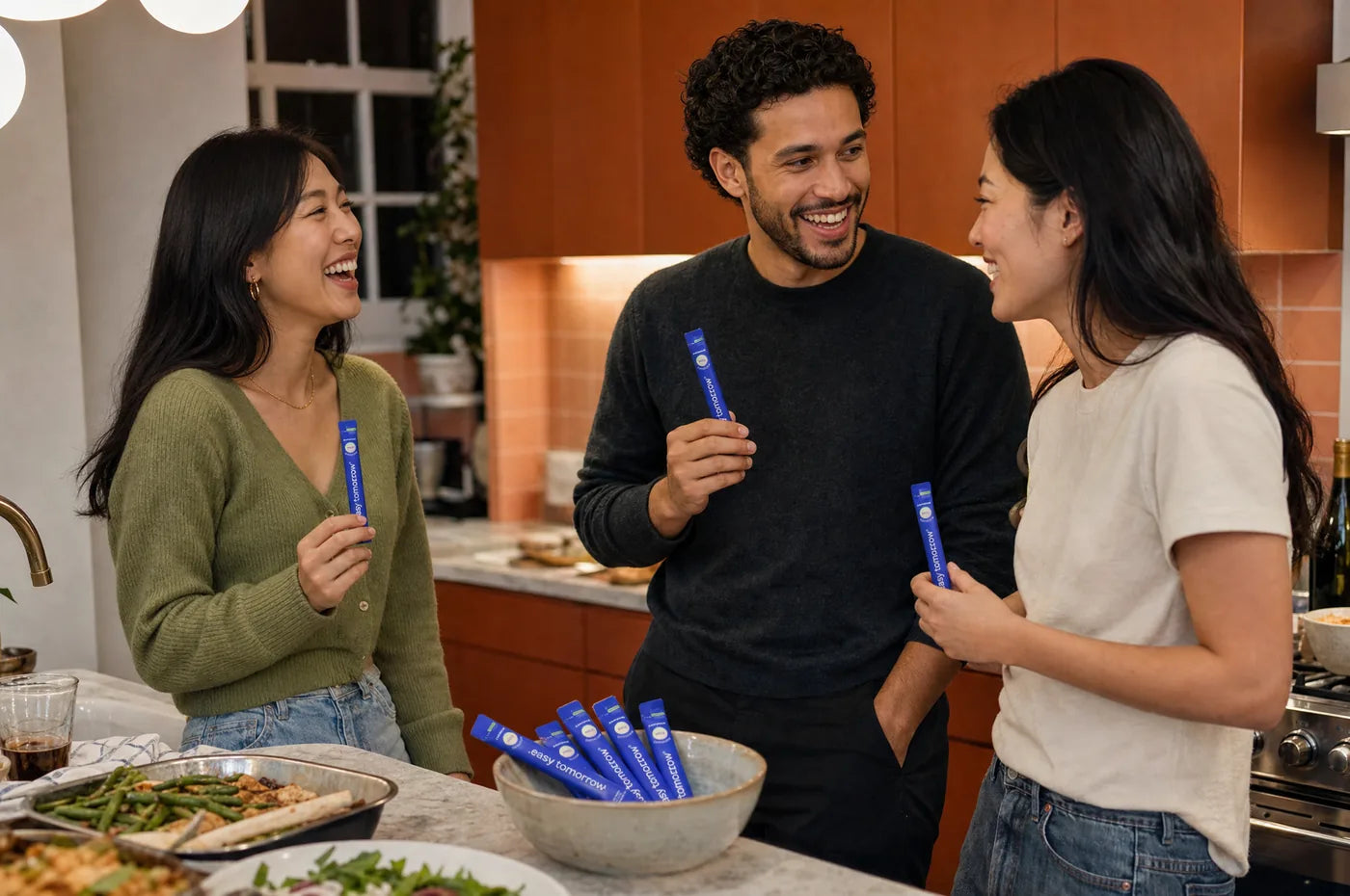Old friends laughing in a kitchen, one handing out Easy Tomorrow sticks