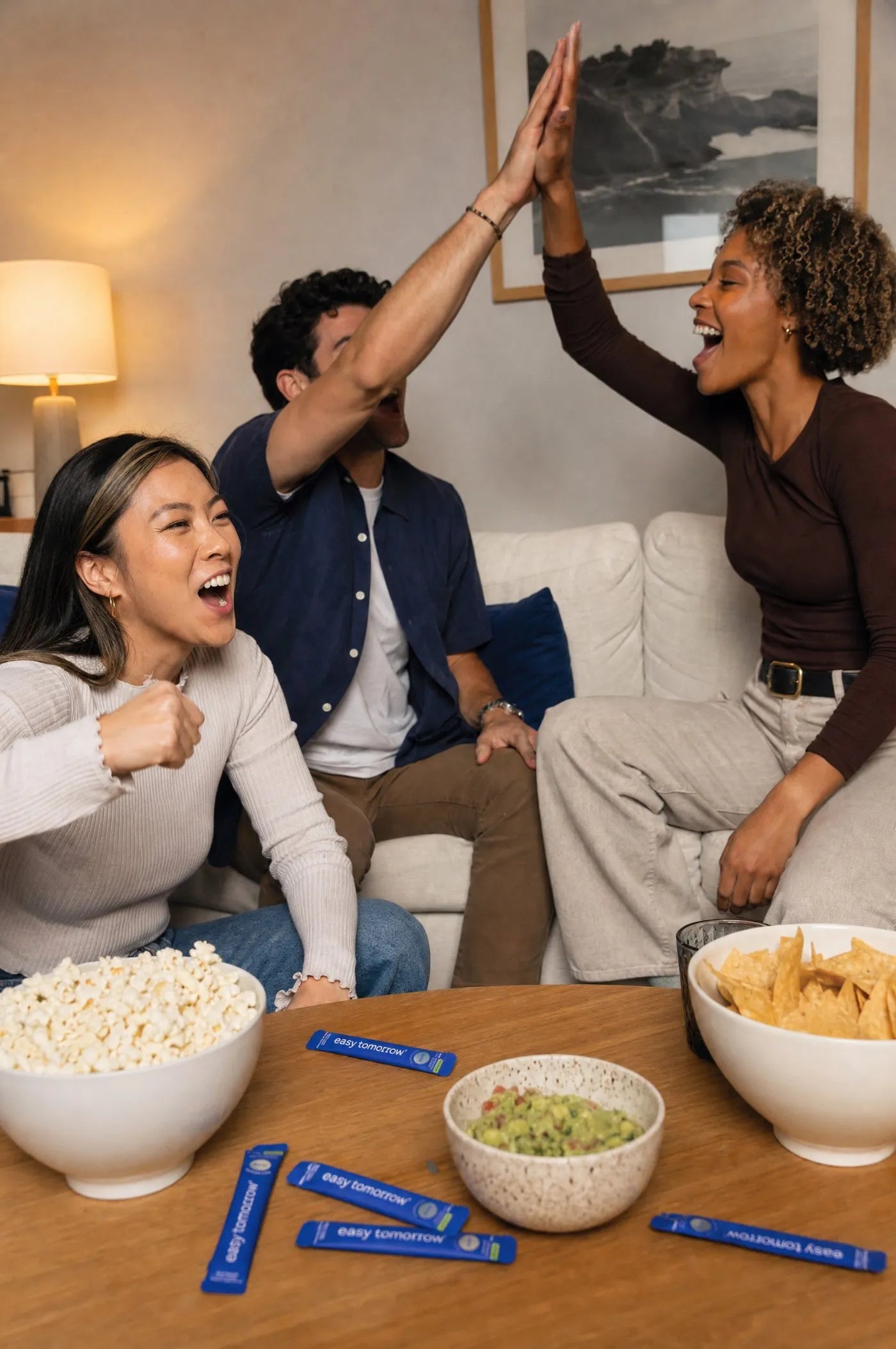 Friends cheering on a couch at a watch party with Easy Tomorrow sticks on the coffee table