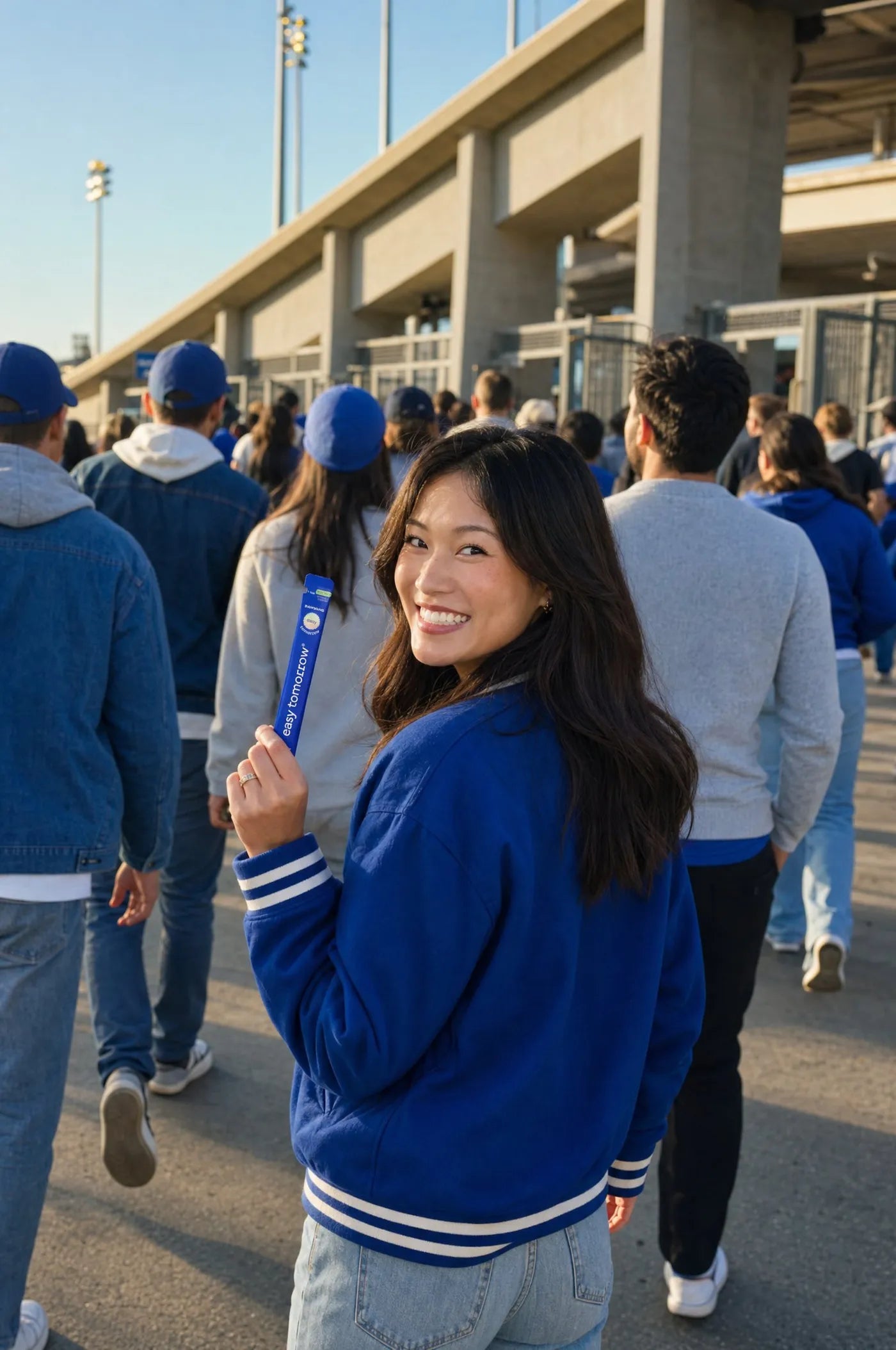 Friends walking into a stadium, one woman looking back holding up an Easy Tomorrow stick